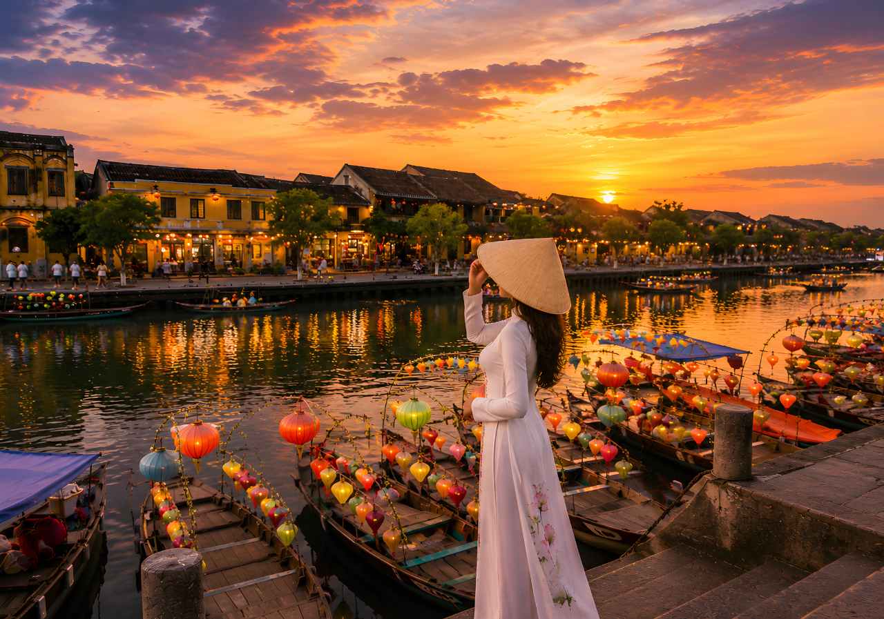 Hoi An Ancient Town lanterns glowing across Thu Bon river with heritage buildings and a woman wearing a traditional Ao Dai dress